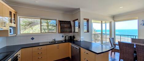 A kitchen with a view of the ocean, a dining area with chairs, and a balcony with a railing.