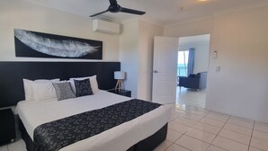 Hotelkamer met een groot bed, een plafondventilator, een decoratie van veren aan de muur en uitzicht op het balkon door een open deur.