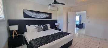 Habitación de hotel con una cama grande, un ventilador de techo, una obra de arte de plumas en la pared y vistas al balcón a través de una puerta abierta.