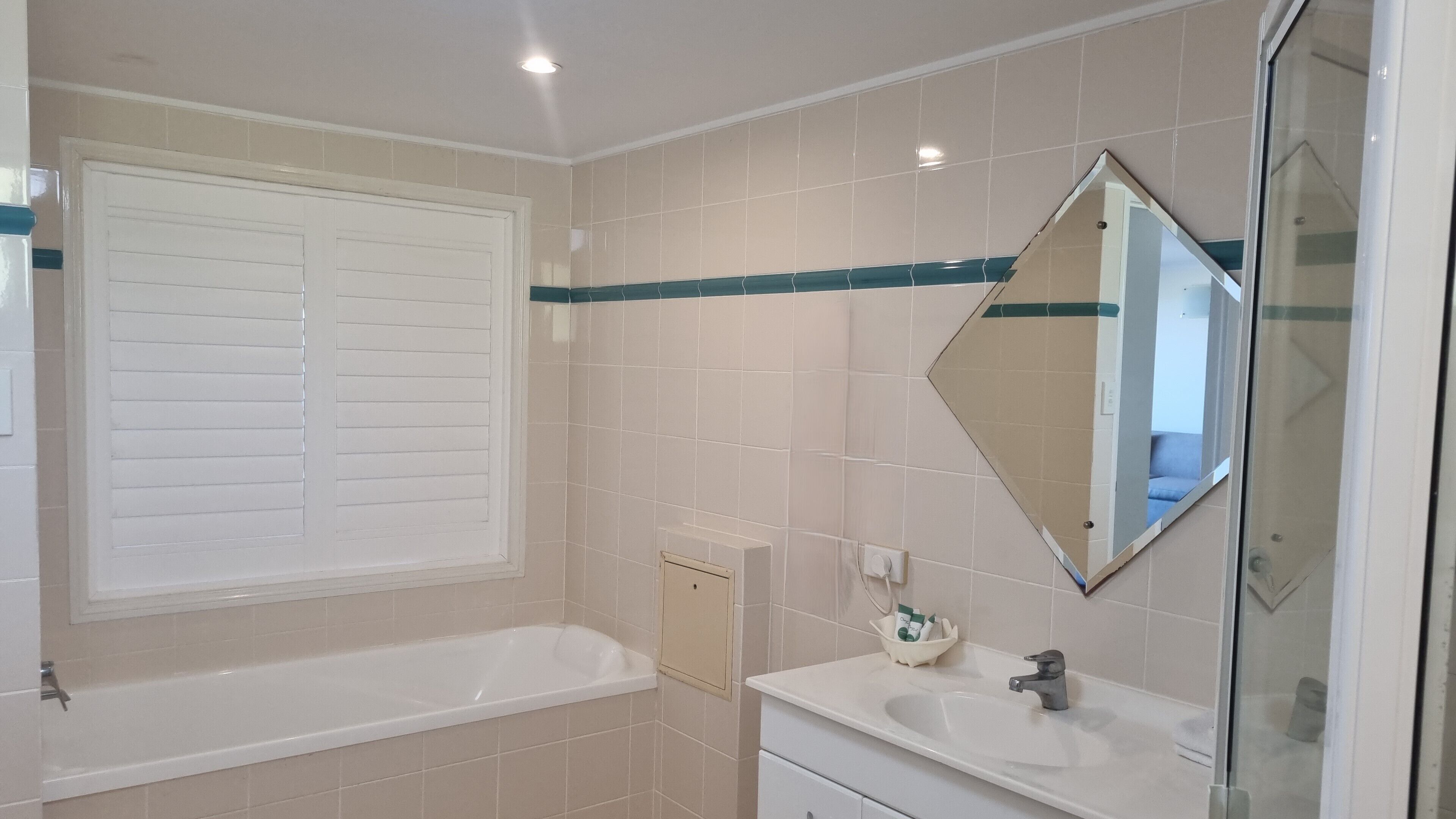 A bathroom with a bathtub, a sink, a mirror, and a window with blinds.