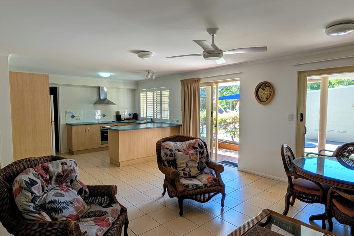 A modern kitchen with a central island, dining area with wicker furniture, and a ceiling fan.