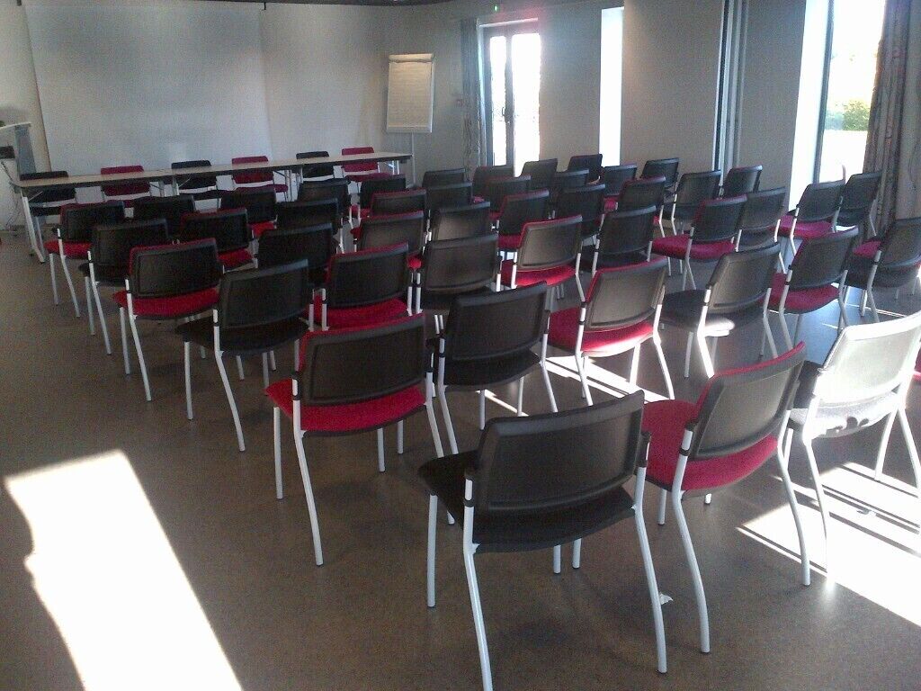A conference room with rows of chairs and tables, large windows, and a projector screen.