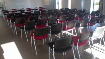 A conference room with rows of chairs and tables, large windows, and a projector screen.