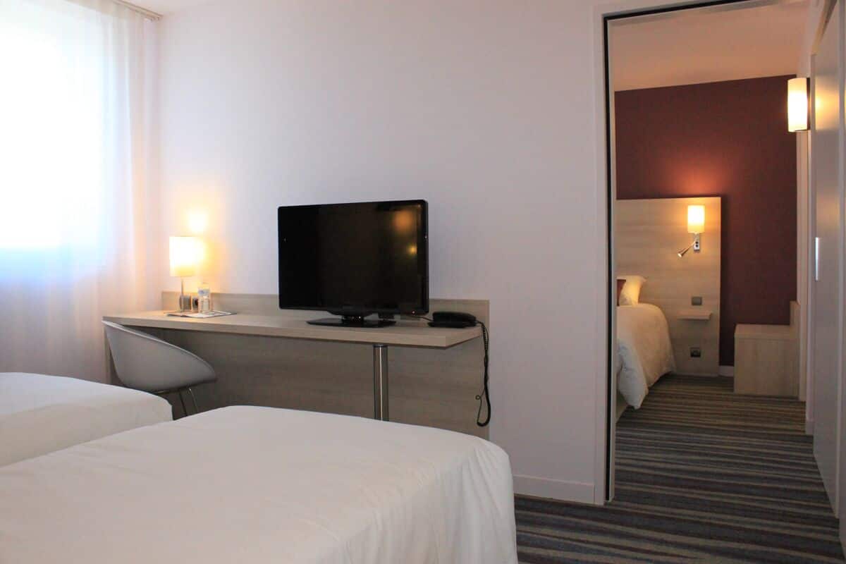 Habitación de hotel con dos camas, un escritorio con televisor, una lámpara y un espejo.