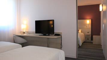 Habitación de hotel con dos camas, un escritorio con televisor, una lámpara y un espejo.
