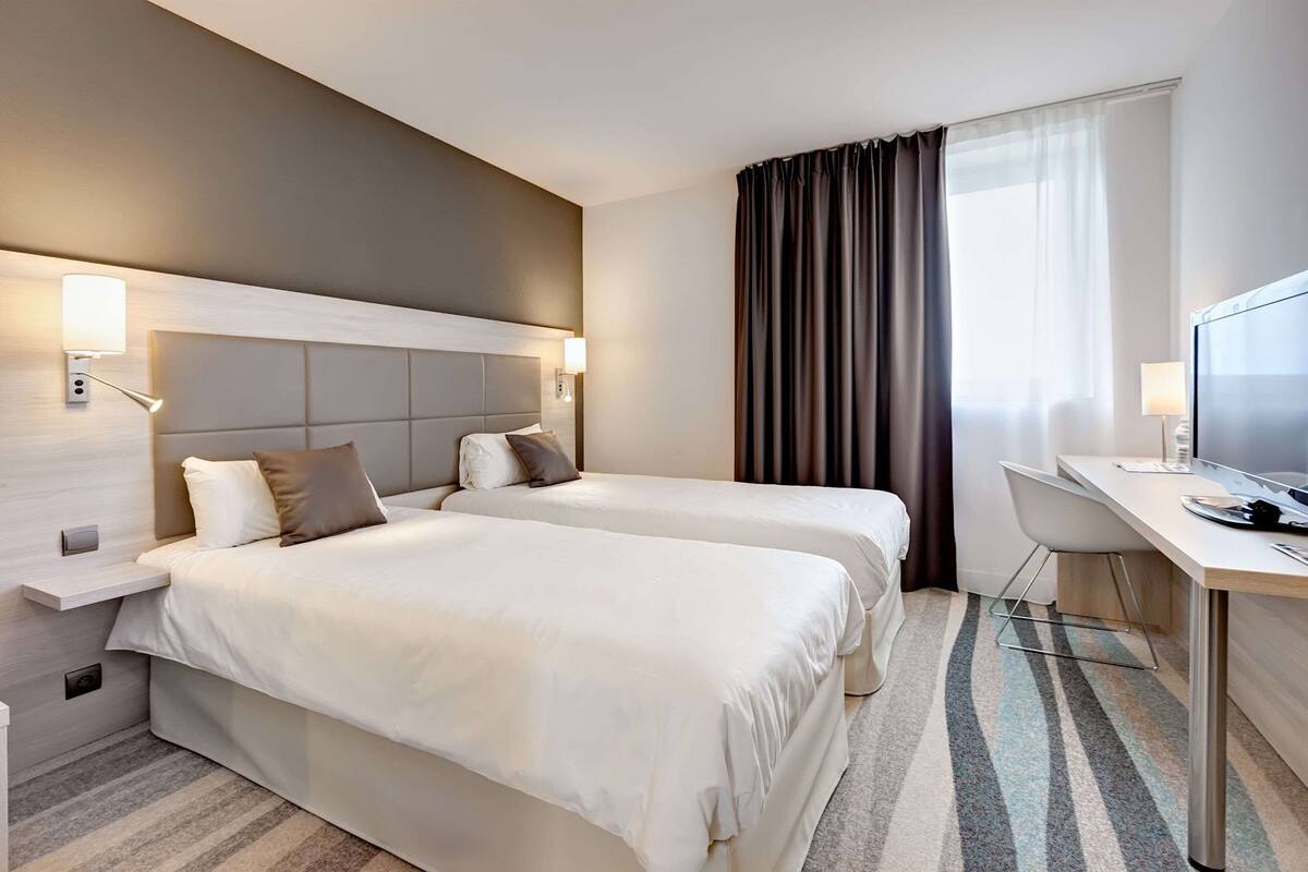 Una habitación de hotel con dos camas, un escritorio, una silla y un televisor.