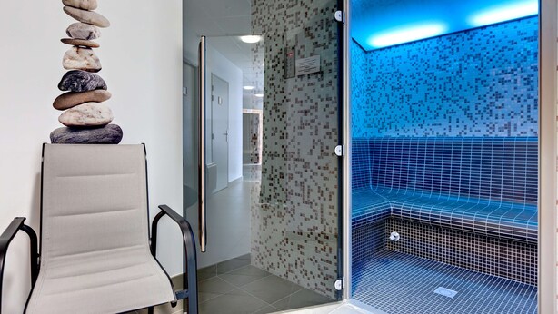 Un área de spa con una pila de piedras, un jacuzzi de vidrio y una zona de estar con una silla.