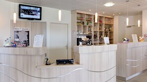 Zona de recepción con un mostrador de madera, un televisor montado en la pared y una estantería con varios objetos, incluyendo botellas y un arreglo floral.