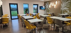 A modern dining area with yellow chairs, white tables, and a TV on the wall. - Brit Hotel Vendee Mer (Les Achards)
