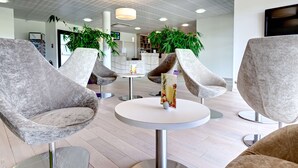Un vestíbulo moderno con sillones tapizados de color gris, mesas redondas y plantas en macetas.