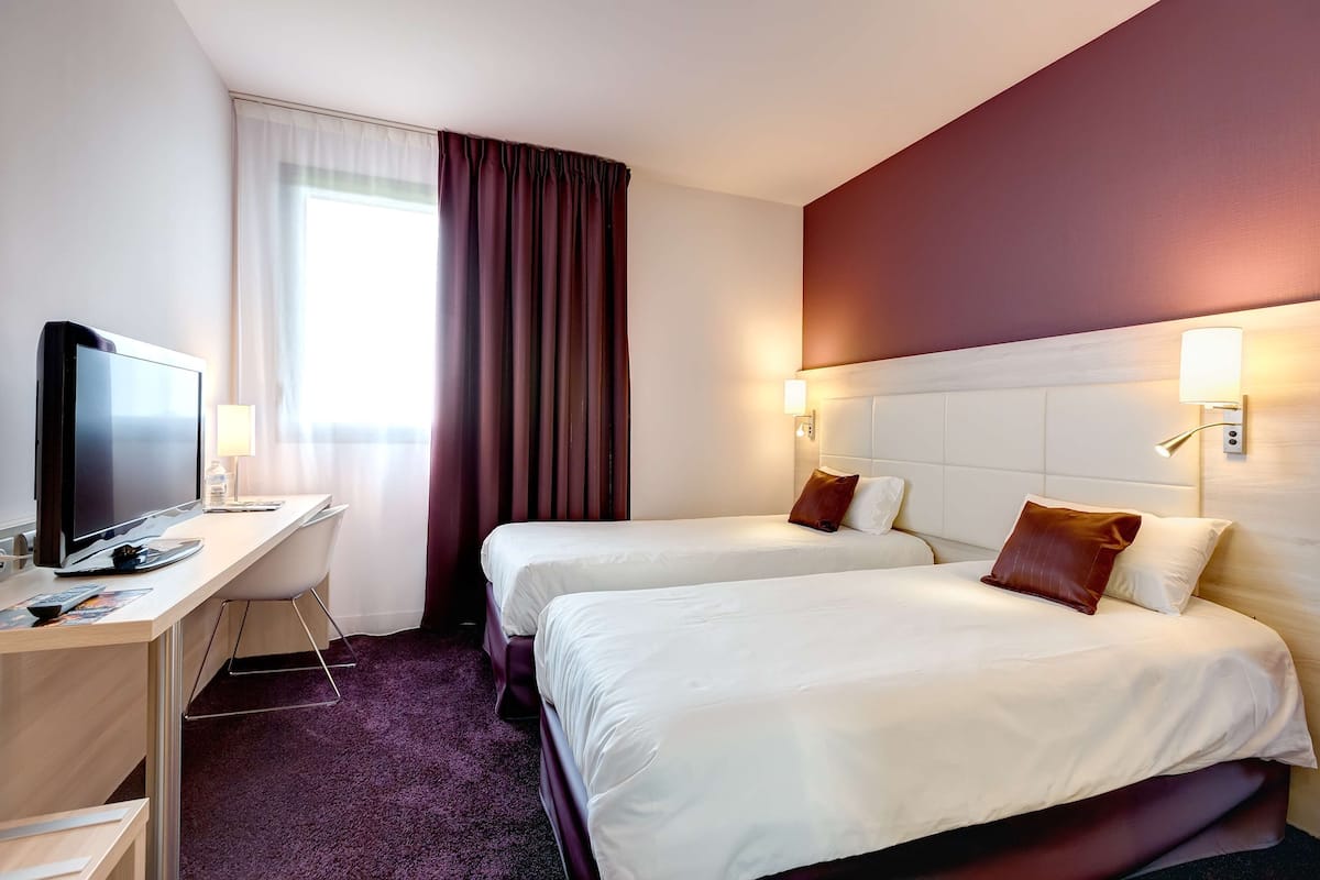 Habitación de hotel con dos camas, un escritorio con computadora y ventana con cortinas.