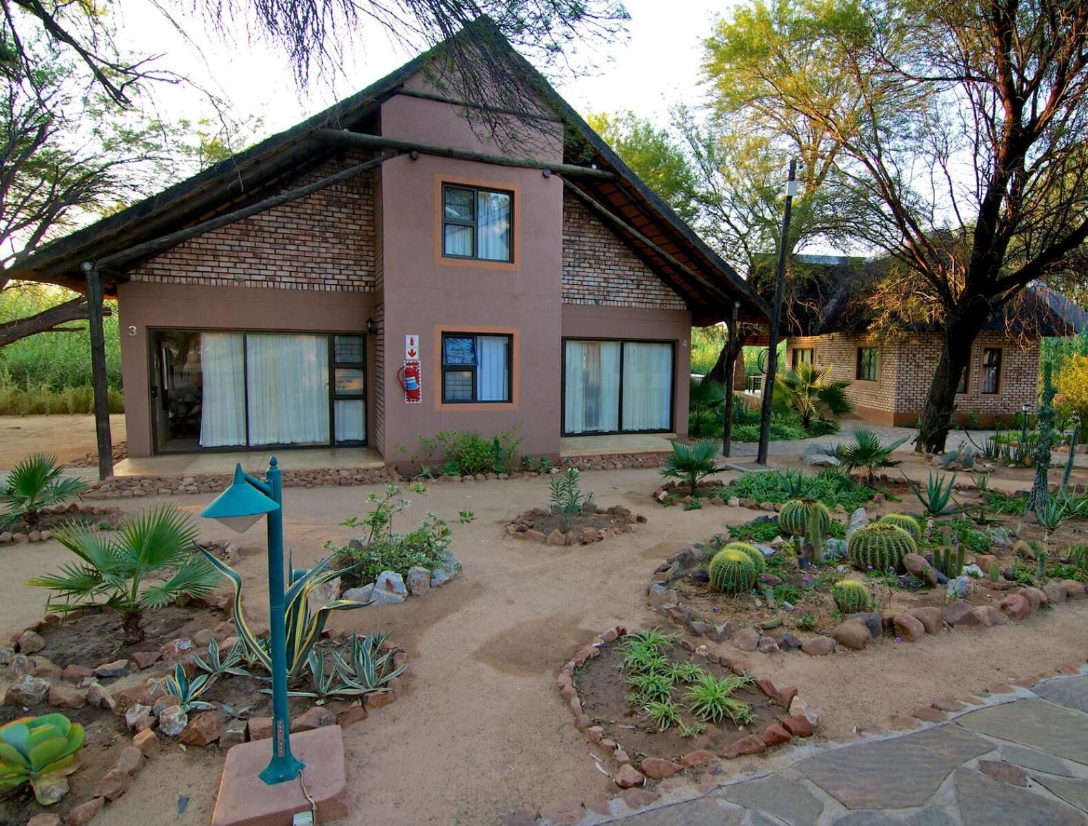 Un edificio de dos plantas con fachada de ladrillo, amplias ventanas y un jardín con diversas plantas y cactus.