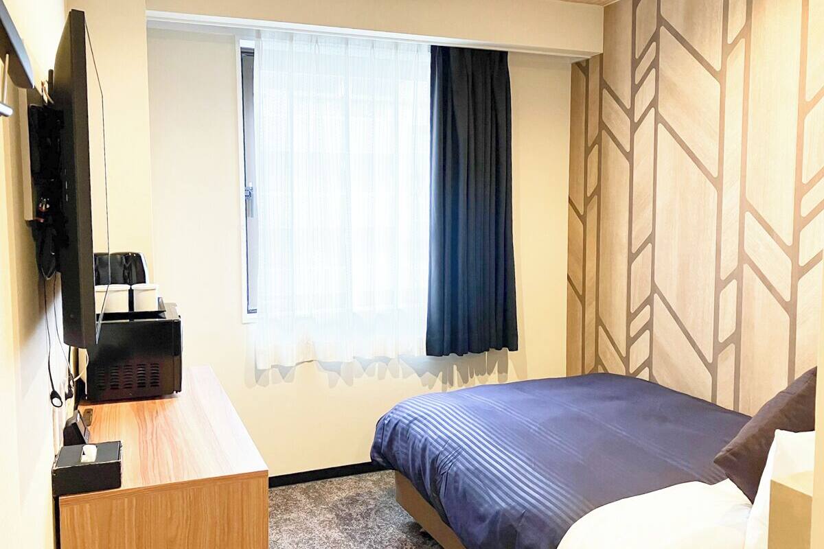 A hotel room with a bed, a desk, a television, and a window with curtains.