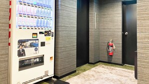 A hotel corridor with a vending machine, a fire extinguisher, and a door. - HOTEL LiVEMAX Chofu-Ekimae (Chofu)