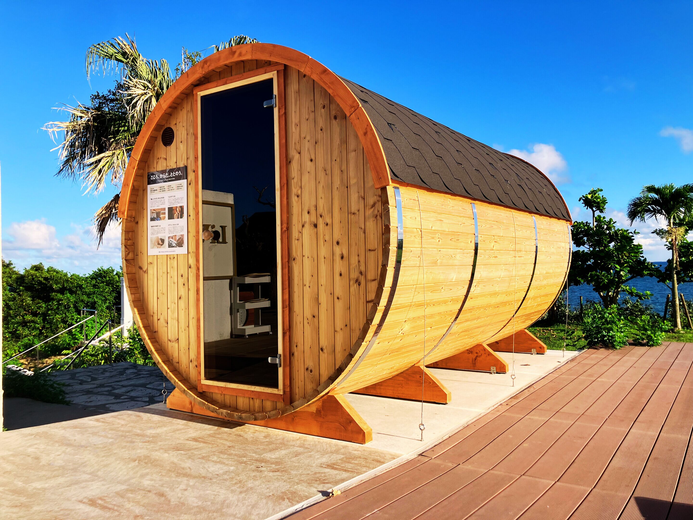 A wooden sauna with a curved roof, situated on a wooden deck with a view of the sea.