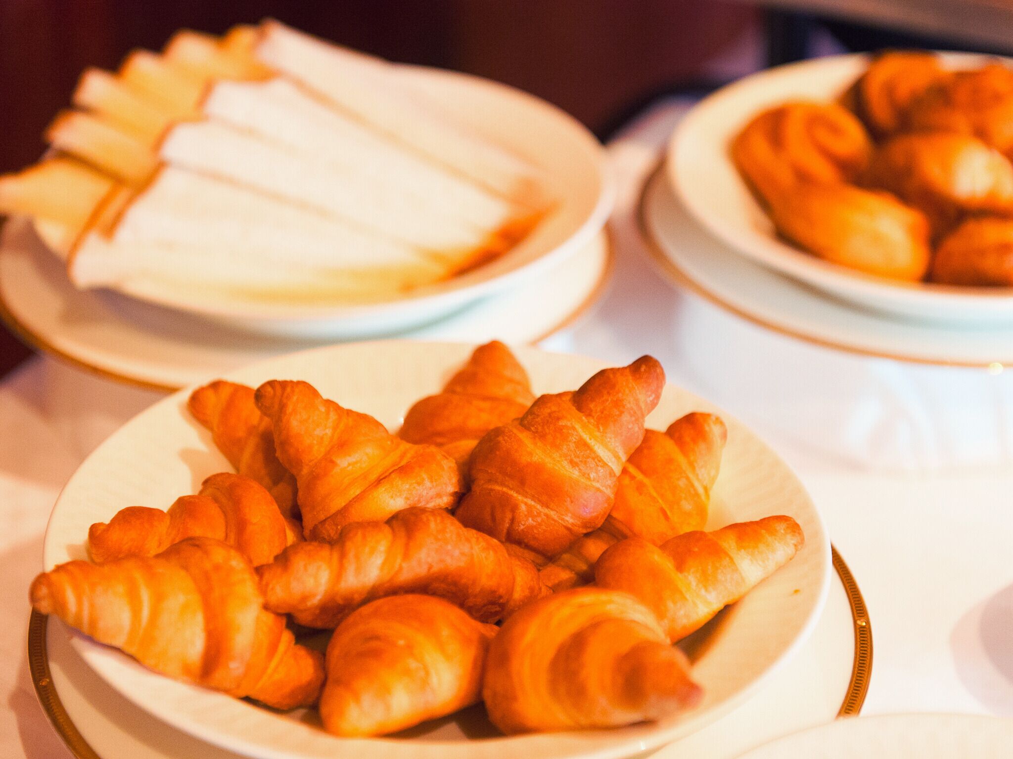 Tres platos de comida, incluyendo cruasanes y otros pasteles, sobre una mesa.