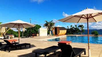 A poolside area with lounge chairs, umbrellas, and a wooden barrel sauna.