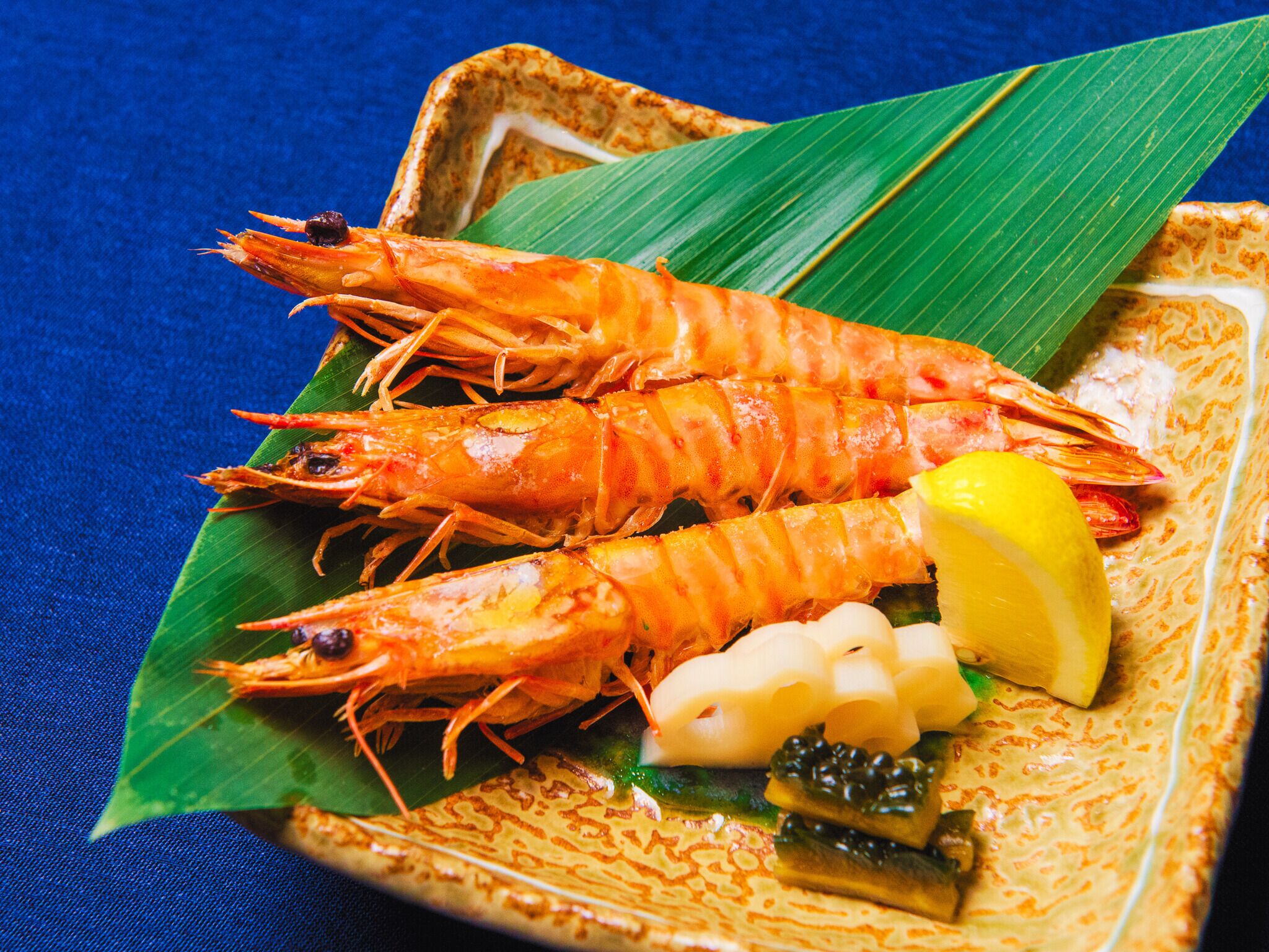 A plate of cooked shrimp with lemon and vegetables on a decorative plate.