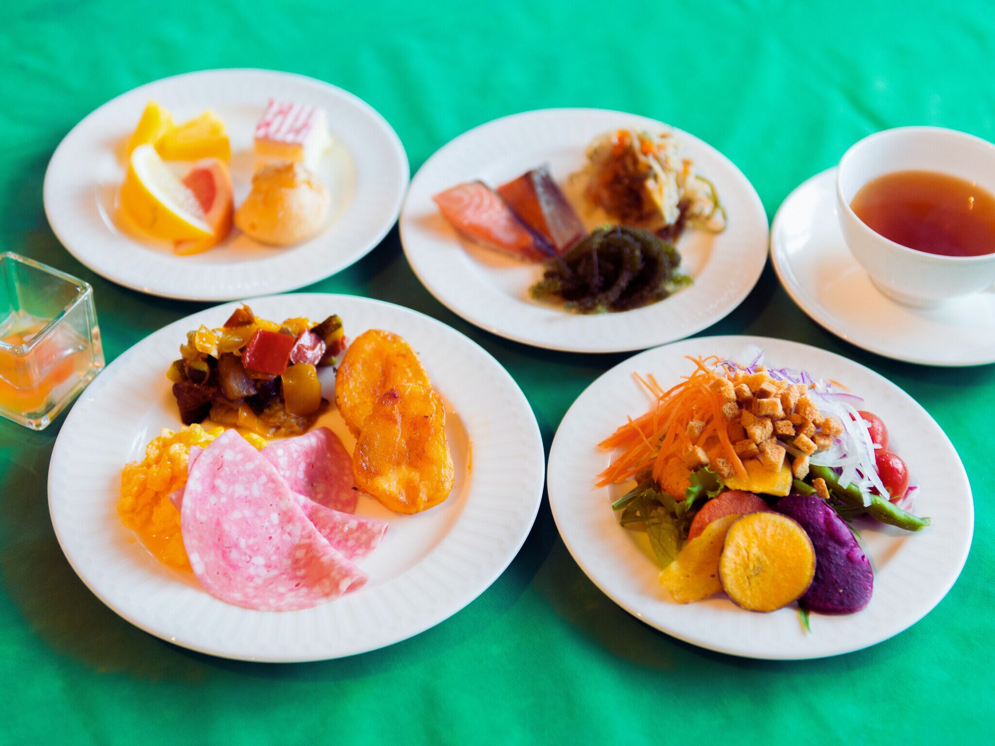 A table with four plates of food, a glass of water, and a cup of tea.
