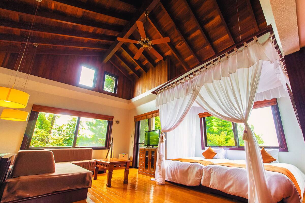 A spacious room with a large bed, a sofa, a wooden table, and a ceiling fan.