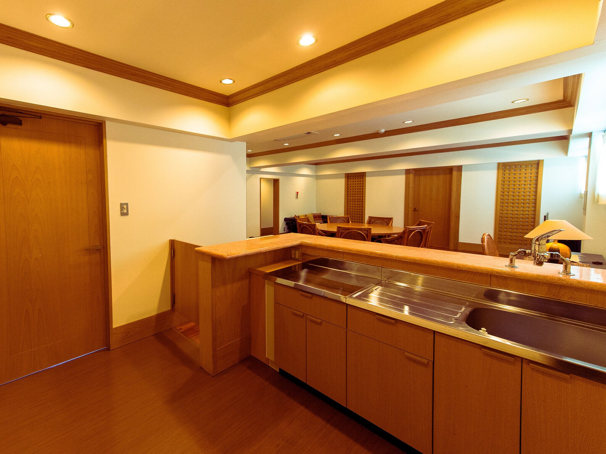 A modern kitchen with wooden cabinets, a stainless steel sink, and a dining area with chairs.