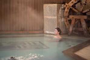 A person in a hot spring with a wooden wheel structure in the background. - Kusatsu Onsen Daitokan (Kusatsu)