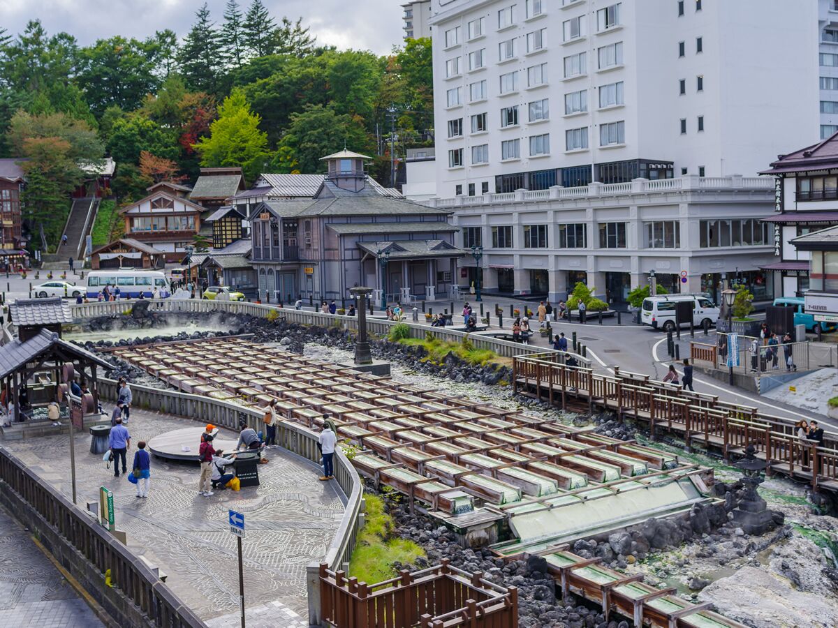 A traditional Japanese onsen with wooden benches and a stone bath area, surrounded by modern buildings and a busy street.