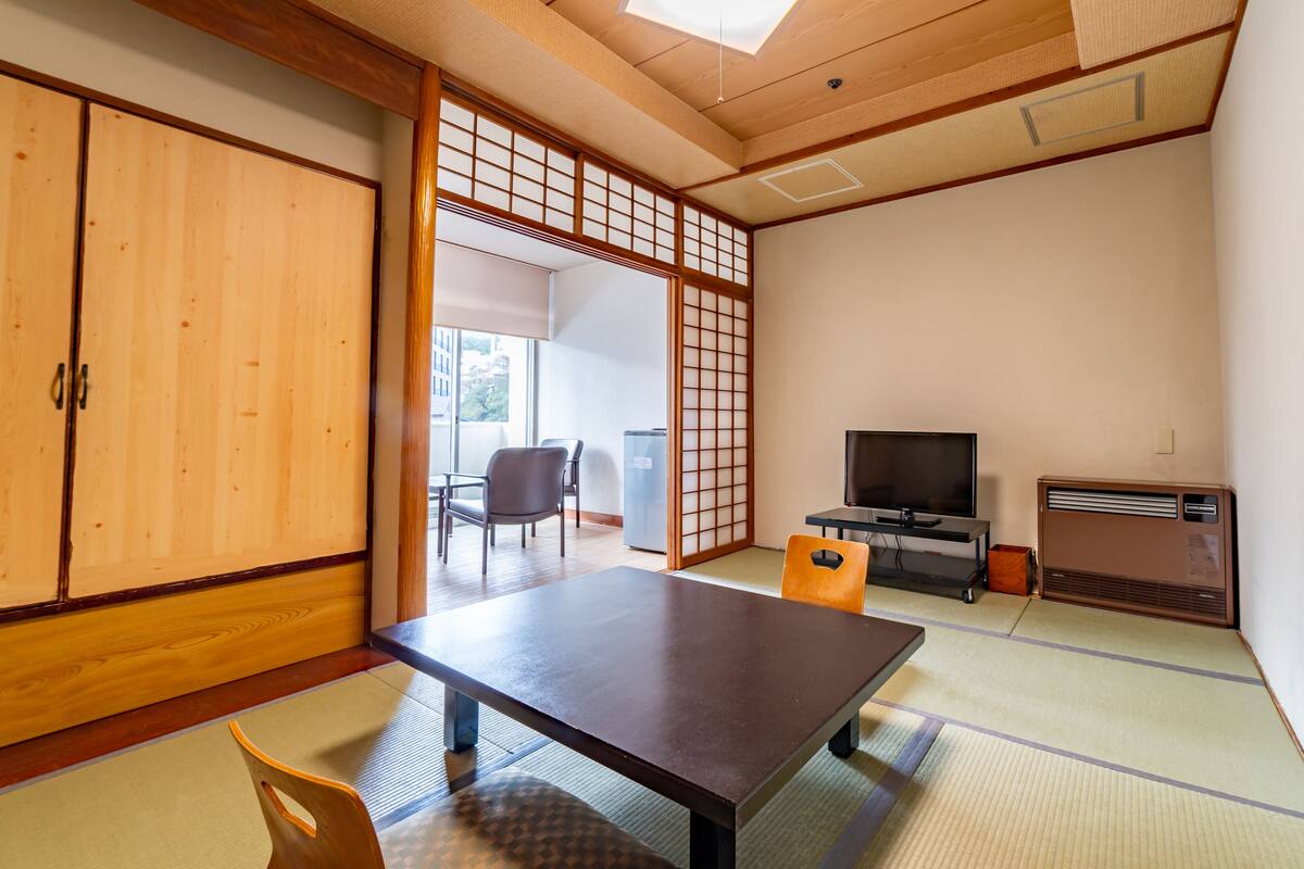 Une pièce de style japonais traditionnel, avec un sol recouvert de tatamis, une table basse, des chaises, un téléviseur et une porte coulissante.