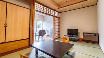 A traditional Japanese room with tatami flooring, a low table, chairs, a television, and a sliding door.