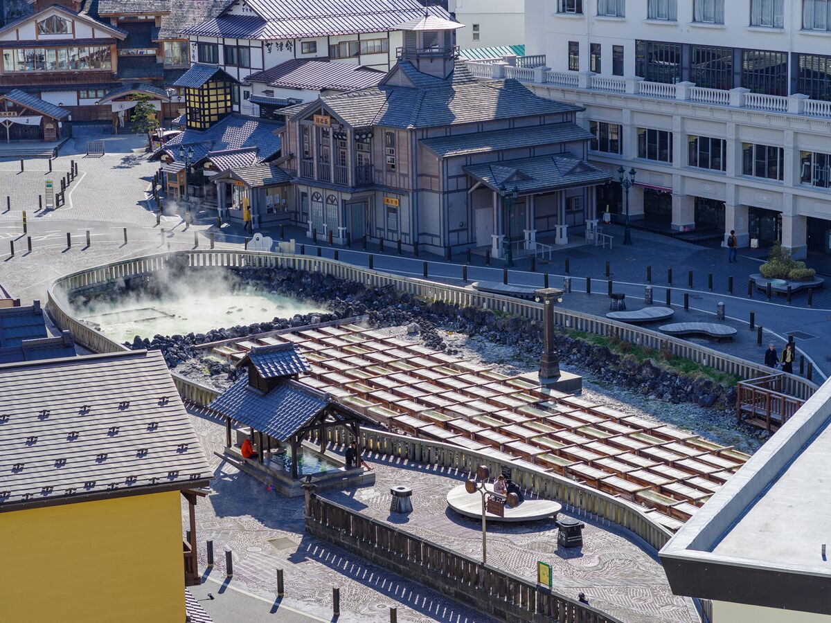 Un balneario japonés tradicional con varias piscinas termales, pasarelas de madera y un pabellón central.