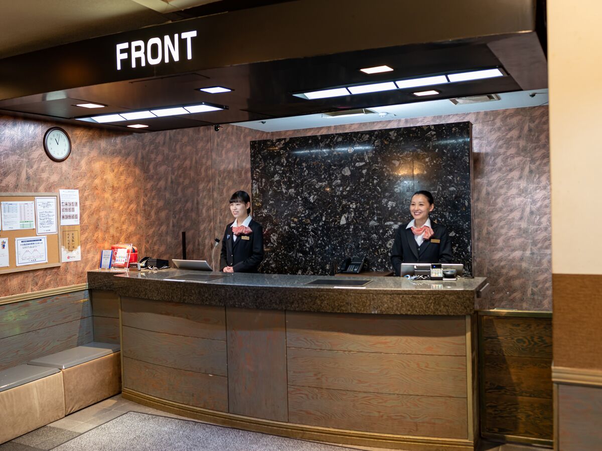 A reception desk with two staff members, a clock, and a bulletin board.