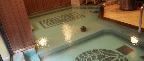 A traditional Japanese onsen with a wooden interior, a stone basin, and a wooden wheel.
