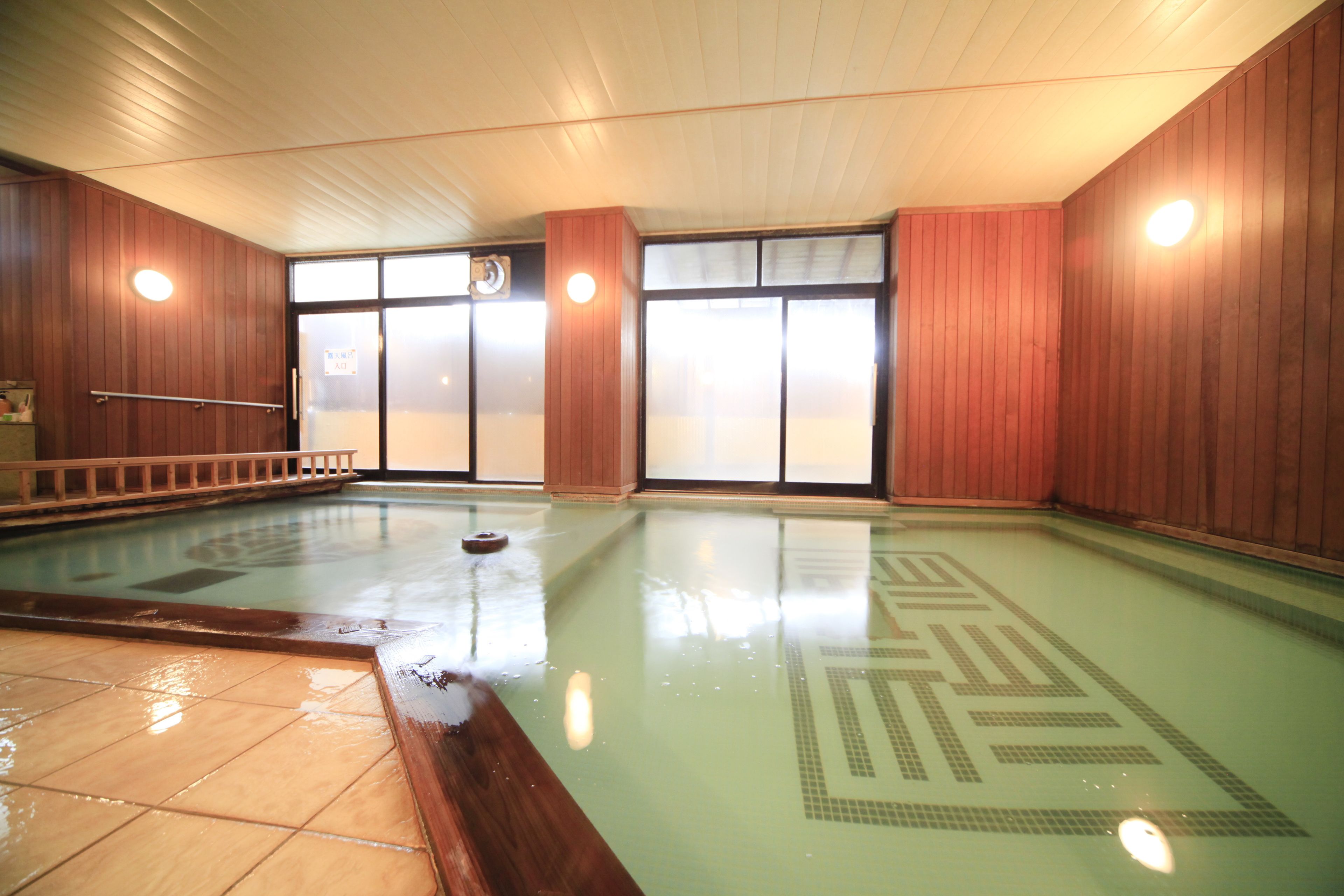 An indoor swimming pool with clear water, wooden walls, and a tiled floor.