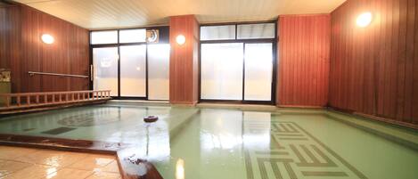 An indoor swimming pool with clear water, wooden walls, and a tiled floor.