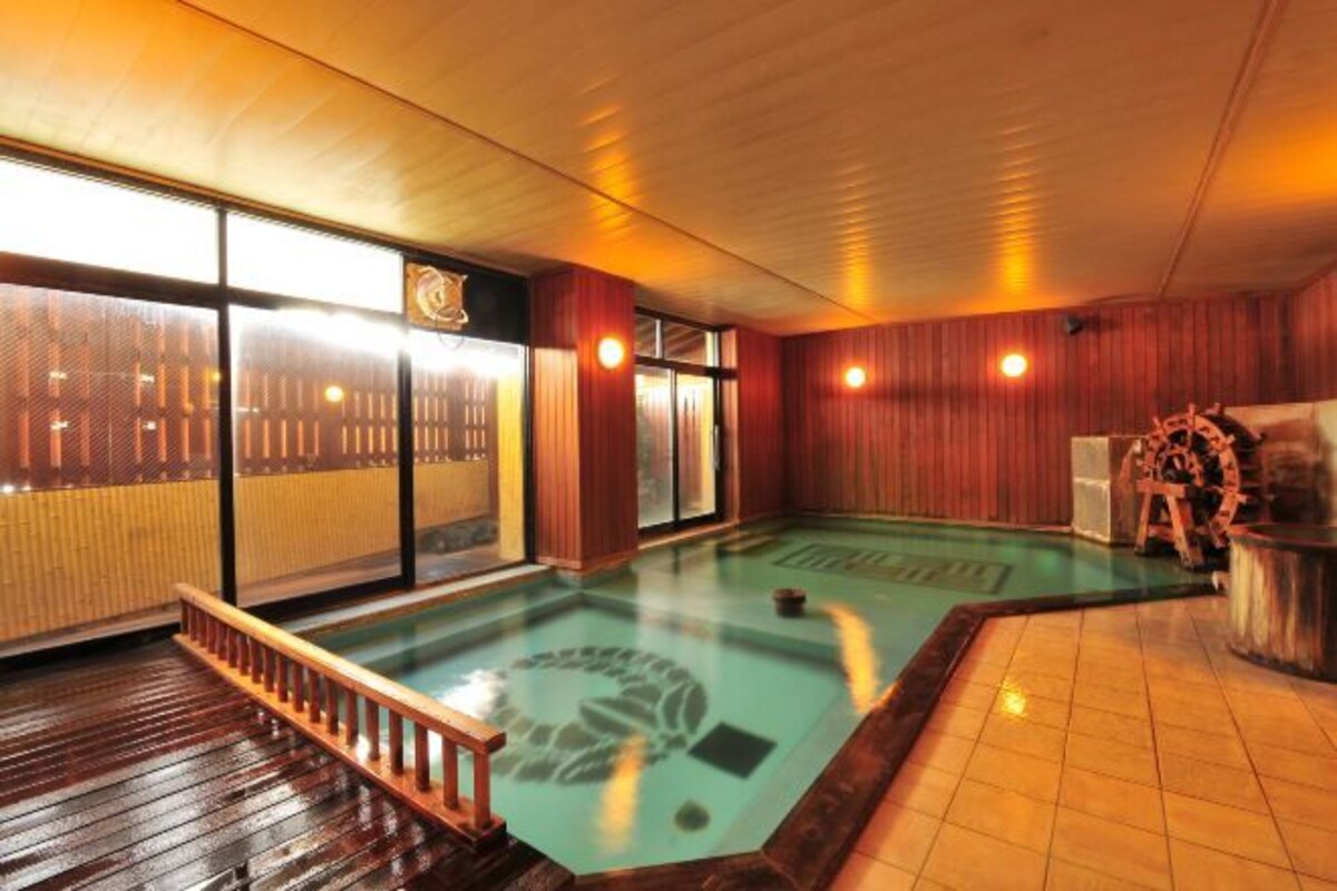 Un onsen japonés tradicional con una terraza de madera, una fuente termal de piedra y un interior de madera.
