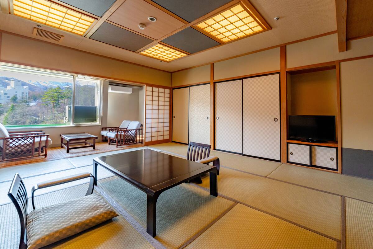 Une pièce de style japonais traditionnel, avec un sol recouvert de tatamis, une table basse, des chaises et un téléviseur.