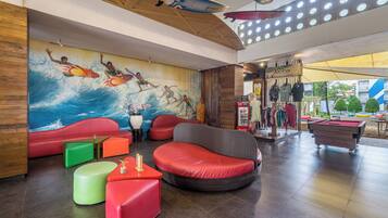 Eine moderne Lobby mit farbenfrohen Sitzgelegenheiten, einem Wandbild von Surfern und einem Billardtisch.