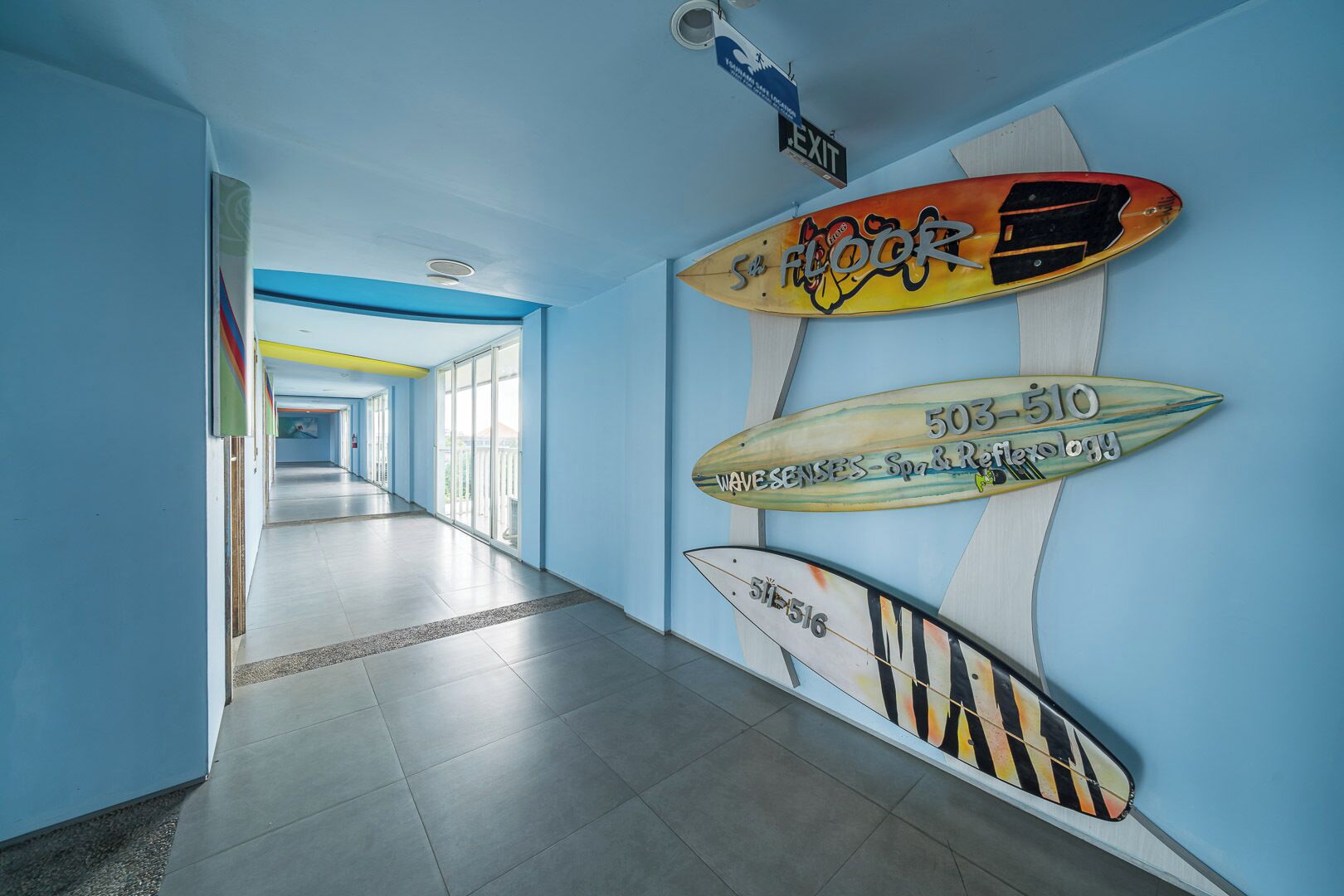 A hallway with blue walls and a tiled floor, decorated with surfboards.