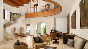 A spacious living area with a curved staircase, comfortable seating, and artwork on the walls. - Hotel Puri Tempo Doeloe (Denpasar)