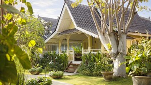 A traditional house with a tiled roof, a porch, and a garden with potted plants and a pathway. - Hotel Puri Tempo Doeloe (Denpasar)