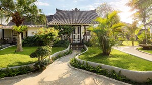 A traditional building with a tiled roof, surrounded by well-maintained gardens and a curved pathway. - Hotel Puri Tempo Doeloe (Denpasar)