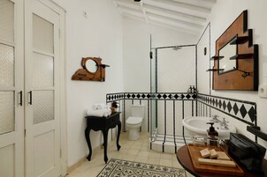 Un baño con inodoro blanco, lavabo, espejo y zona de ducha.