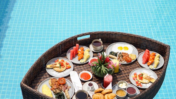 A dining table with various dishes and drinks on a poolside setting. - Hotel Puri Tempo Doeloe (Denpasar)