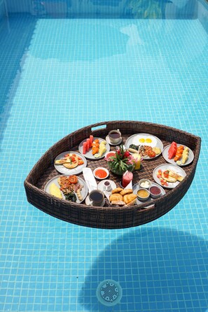 A dining table with various dishes and drinks on a poolside setting. - Hotel Puri Tempo Doeloe (Denpasar)