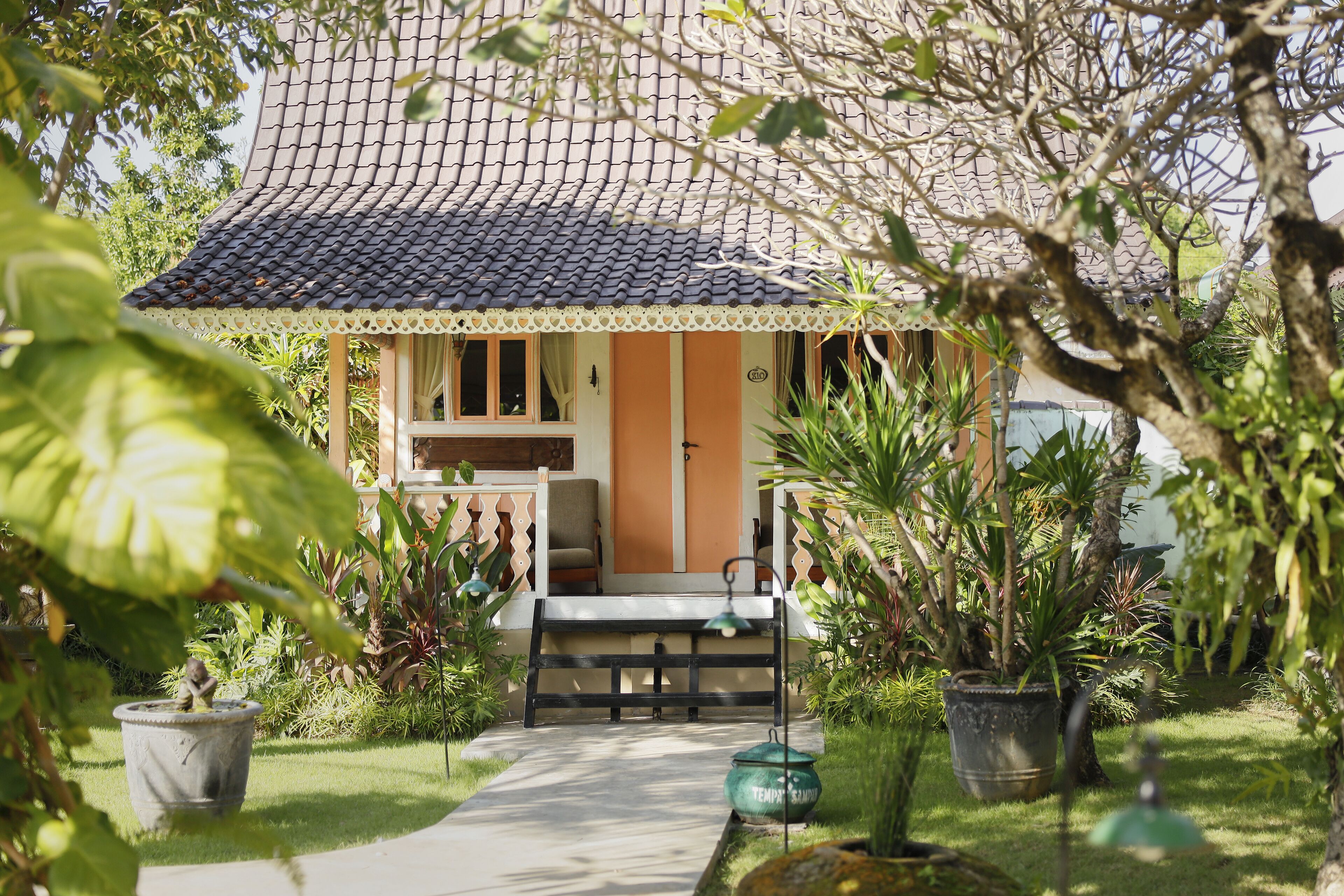 A house with a tiled roof, a porch with a bench, and potted plants.