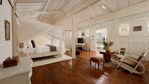 A bedroom with a canopy bed, a desk, a TV, and a seating area with chairs. - Hotel Puri Tempo Doeloe (Denpasar)