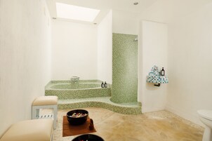 A bathroom with a green mosaic shower, a white toilet, and a small sink with a checkered soap dispenser.