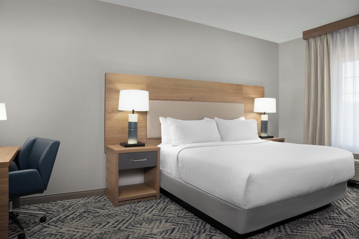 A hotel room with a large bed, two bedside tables with lamps, a desk with a chair, and a patterned carpet.