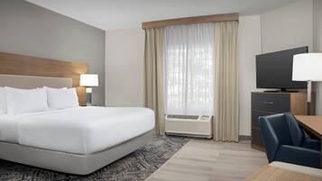 A hotel room with a bed, a desk, a chair, a television, and an air conditioning unit.