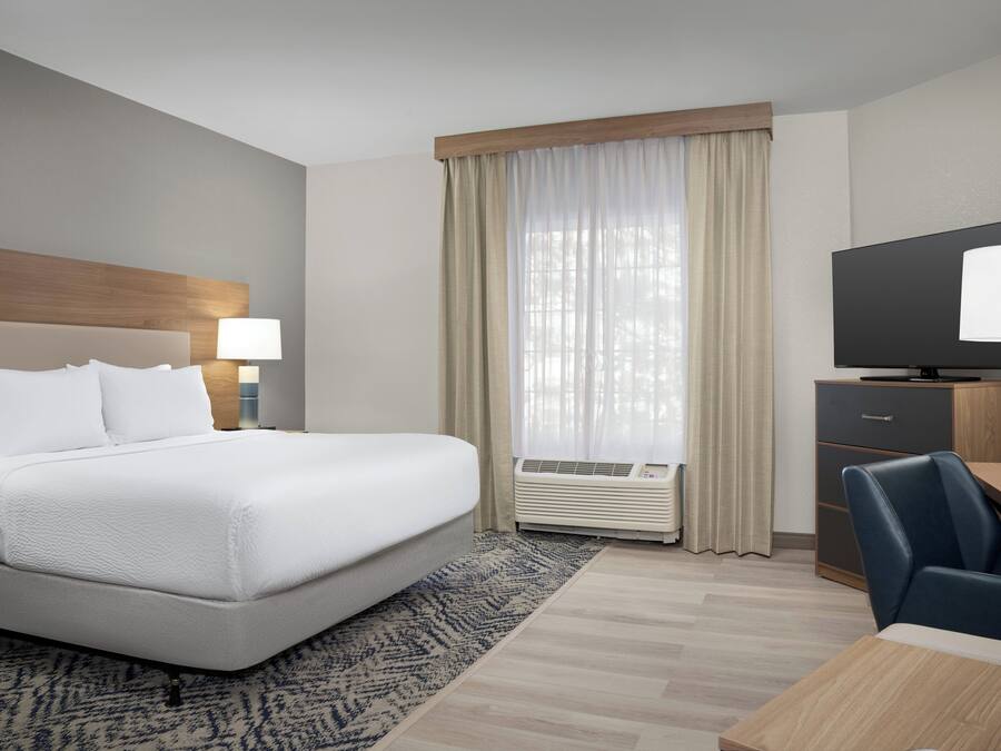 A hotel room with a bed, a desk, a chair, a television, and an air conditioning unit.